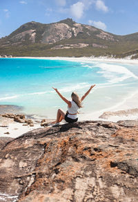 Rear view of woman jumping at beach against sky
