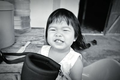 Portrait of cute baby girl holding container while clenching teeth outdoors