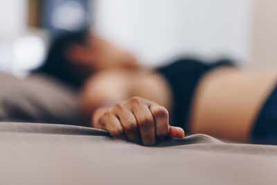 Close-up of woman holding sheet while lying on bed at home