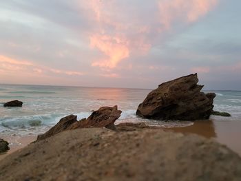 Rocks on beach against sky during sunset