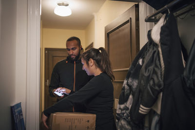 Female customer signing on mobile phone for delivery from male worker at doorway