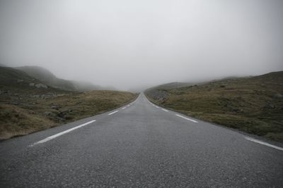 Country road leading towards mountains against sky