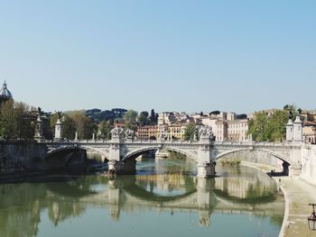 Bridge over river by buildings against clear sky