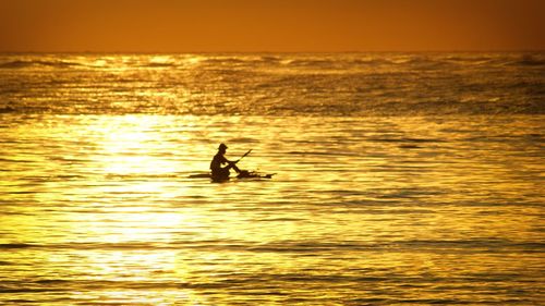 Silhouette man in sea against sky during sunset