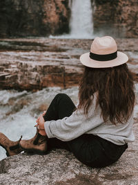 Woman wearing hat sitting outdoors near waterfall at crescent falls, alberta 