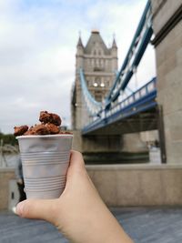 Midsection of person holding ice cream against bridge