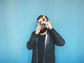 Portrait of a man using analog camera against blue background