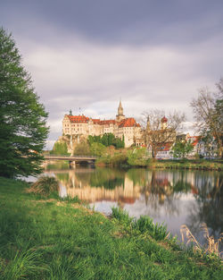 View of buildings by lake against cloudy sky