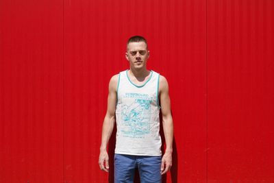 Portrait of young man standing against red wall