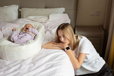 Sad woman leaning by baby on bed at home