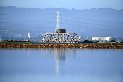 Electricity pylon by bridge against sky