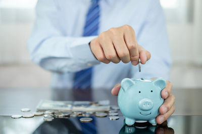 Midsection of businessman putting coin in piggy bank