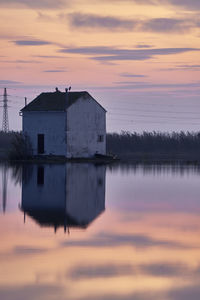 Reflection of house on lake against sky during sunset