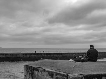 Rear view of man sitting on shore against sky
