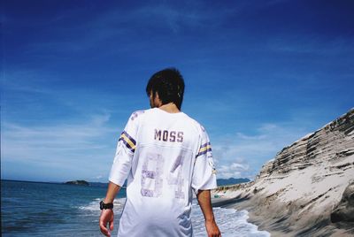 Rear view of man standing on beach against sky