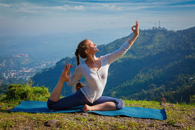 Rear view of woman doing yoga on mountain against sky