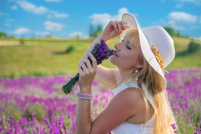 Woman wearing hat smelling flowers at field