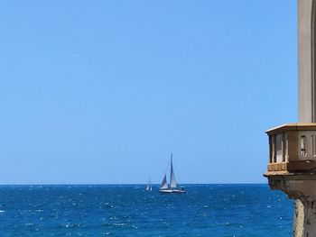 Sailboat sailing in sea against clear blue sky