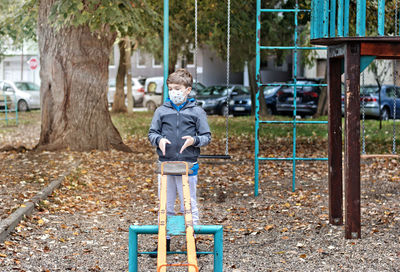 Boy feeling bored while playing alone at  playground and wearing face mask due to covid-19 pandemic.