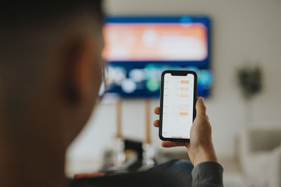 Teenage boy using smart phone app while watching tv in living room at home