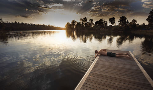 Shirtless man practicing yoga on pier against sky during sunset