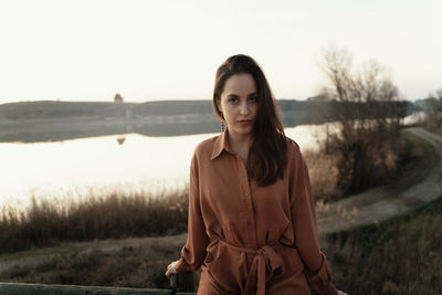 Portrait of young woman standing by lake against sky