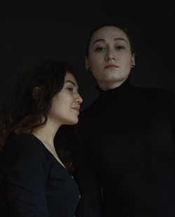 Portrait of sisters looking away against black background