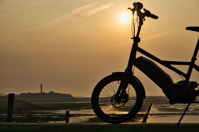 Silhouette bicycle parked on street against sky during sunset