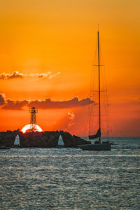 Silhouette sailboat sailing on sea against orange sky