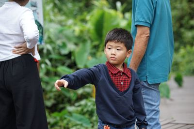 Boy pointing while standing with parents against plants