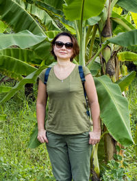 Portrait of woman wearing sunglasses while standing against banana tree