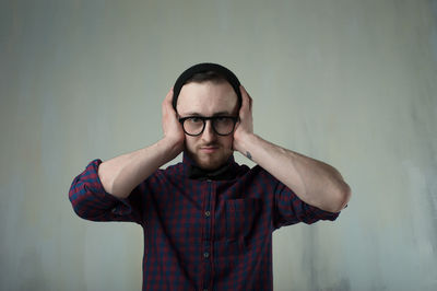 Portrait of young man covering ears against wall