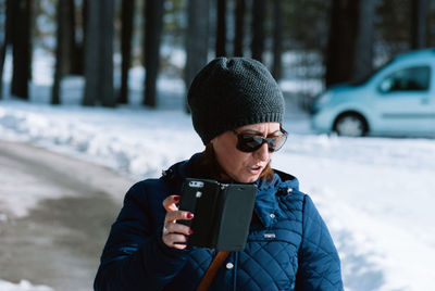 Mature woman holding mobile phone while standing by snow covered field