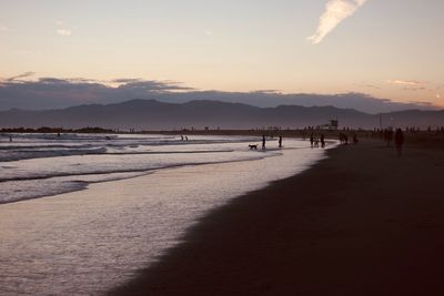 Silhouette people at beach against sky during sunset