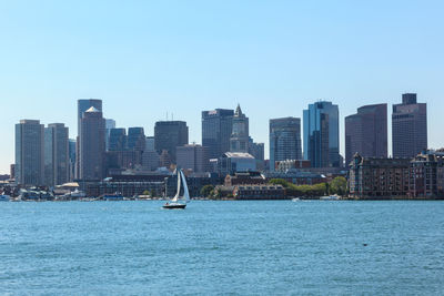 Sailboats in sea by modern buildings against clear sky