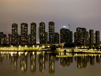 Illuminated buildings by river against sky at night