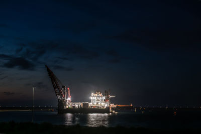 Illuminated commercial dock by sea against sky at night