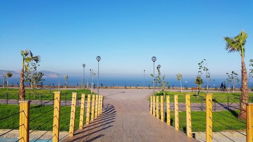 Footpath by street against clear blue sky