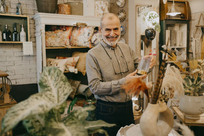 Happy senior male owner showing glass decor at home interior store