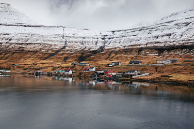 Breathtaking scenery of residential houses located near river in highland valley with mountains covered with snow on faroe islands