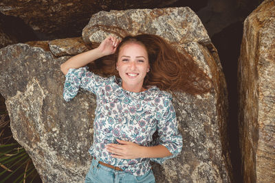 Portrait of smiling young woman lying down on rock