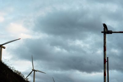 Low angle view of wind turbines against cloudy sky