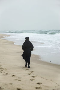A lonely girl in a black long coat on the coast of a stormy sea in a storm