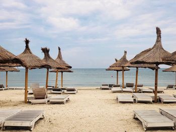 Lounge chairs and thatched roofs at beach against sky