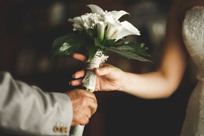 Cropped hand of bridegroom giving bouquet to bride