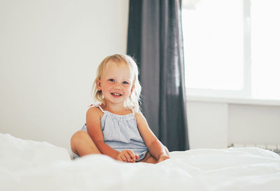 Portrait of cute girl sitting on bed at home