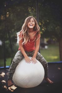 Smiling girl sitting over fitness ball on trampoline