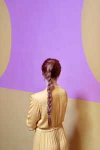 Portrait of young woman in yellow, standing against pink wall