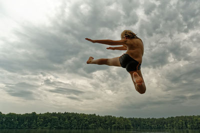 Full length of shirtless boy gesturing while jumping against sky