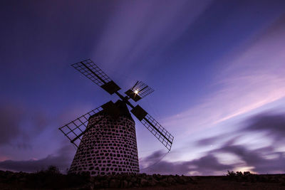 Low angle view of traditional windmill on field against dramatic sky during sunset
